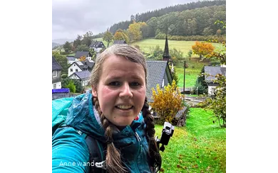 Anne macht ein Selfie im Regen. Hinter ihr befindet sich das Dorf Wirme im Tal