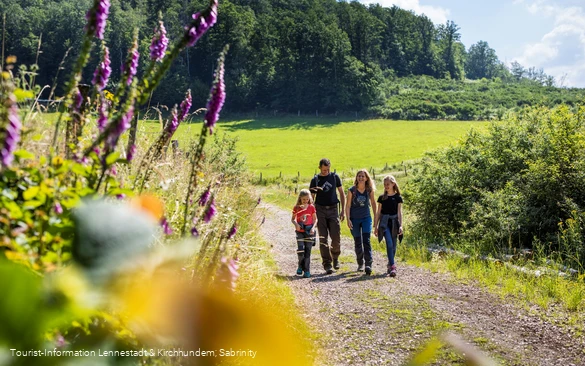 Familie wandert auf Wanderweg zwischen bunt blühenden Blumen und Wiesen.